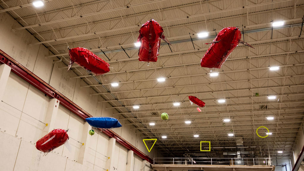 Red and blue balloon air blimps move through a geometric obstacle course