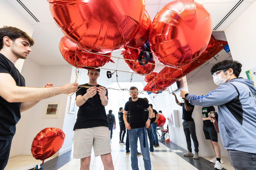 Male students hold and operate a red balloon BLIMP in the middle of a busy school hallway